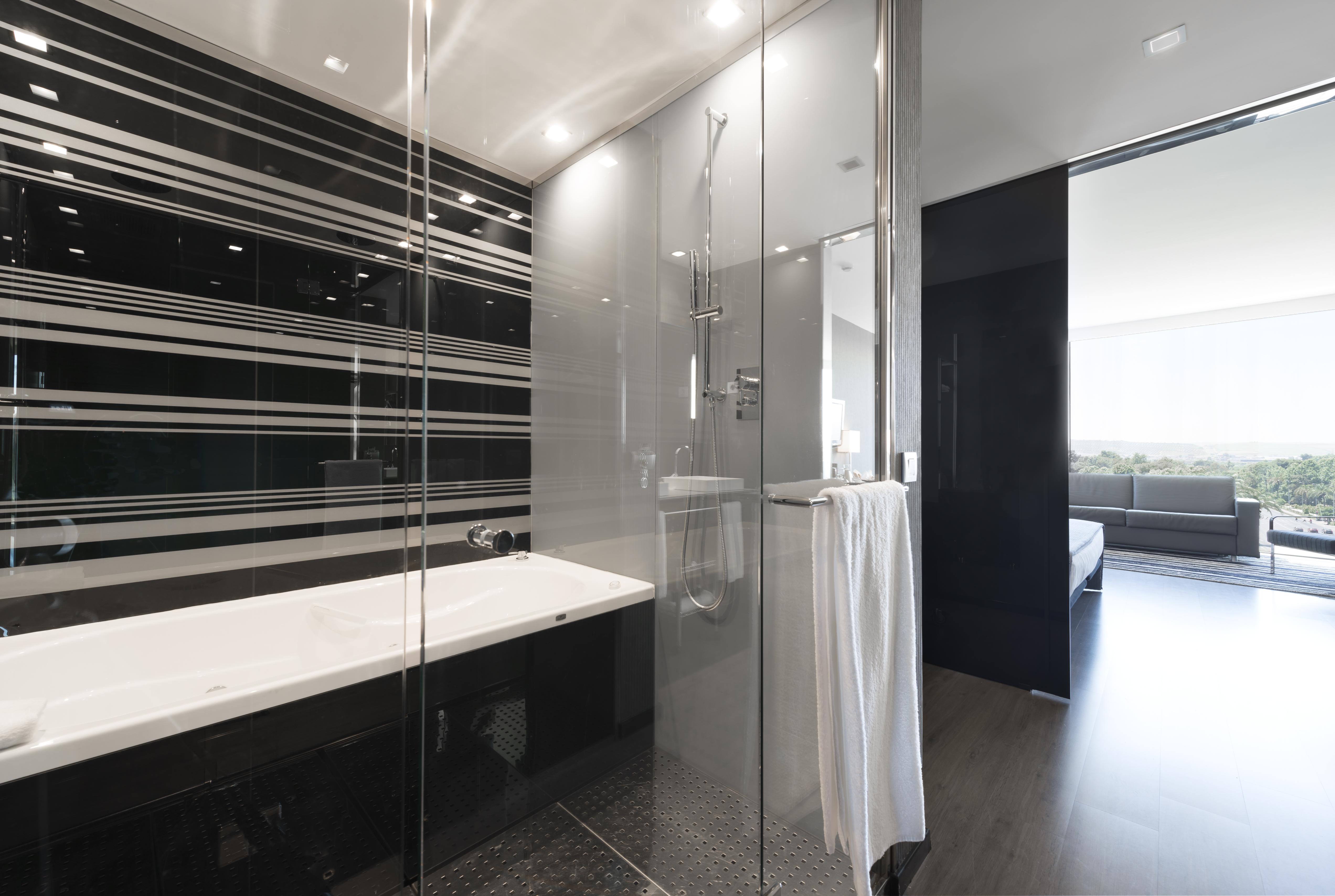فندق يوروستارز بالاس قرطبة المظهر الخارجي الصورة The photo shows a modern bathroom featuring a sleek design. On one side, there is a glass-enclosed shower with contemporary fixtures. Adjacent to it, there's a stylish bathtub with a clean, white surface. The walls are decorated with a striking patte