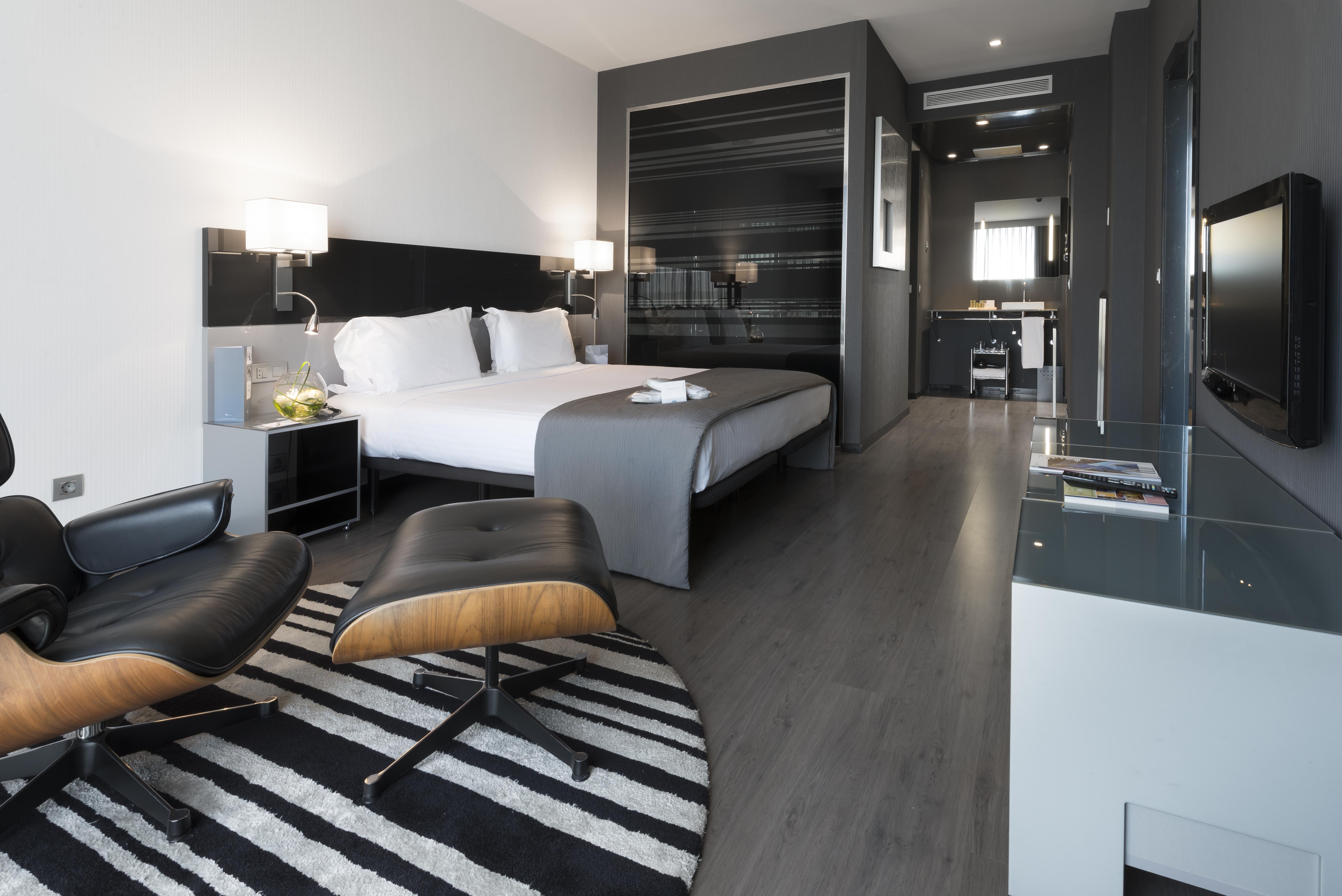 فندق يوروستارز بالاس قرطبة المظهر الخارجي الصورة The photo shows a modern hotel room featuring a king-sized bed with light-colored linens and dark accent walls. There are stylish bedside tables with lamps, and a comfortable lounge chair paired with an ottoman placed on a striped rug. The room also 