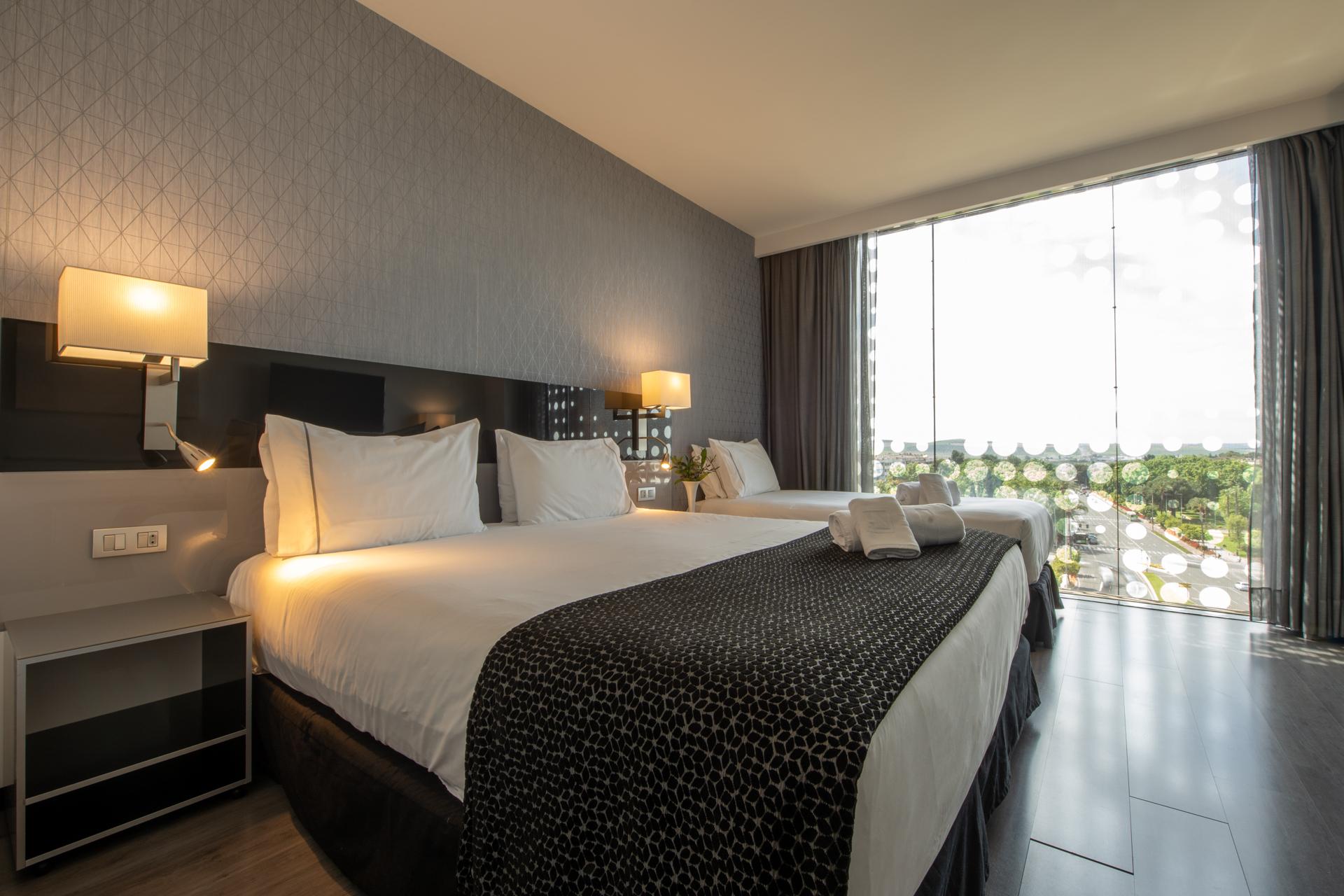 فندق يوروستارز بالاس قرطبة المظهر الخارجي الصورة The photo shows a modern hotel room featuring two large beds with white linens and dark patterned bedspreads. Each bed has a set of pillows and a decorative cushion. There are bedside lamps on either side of the beds, and a contemporary piece of furn