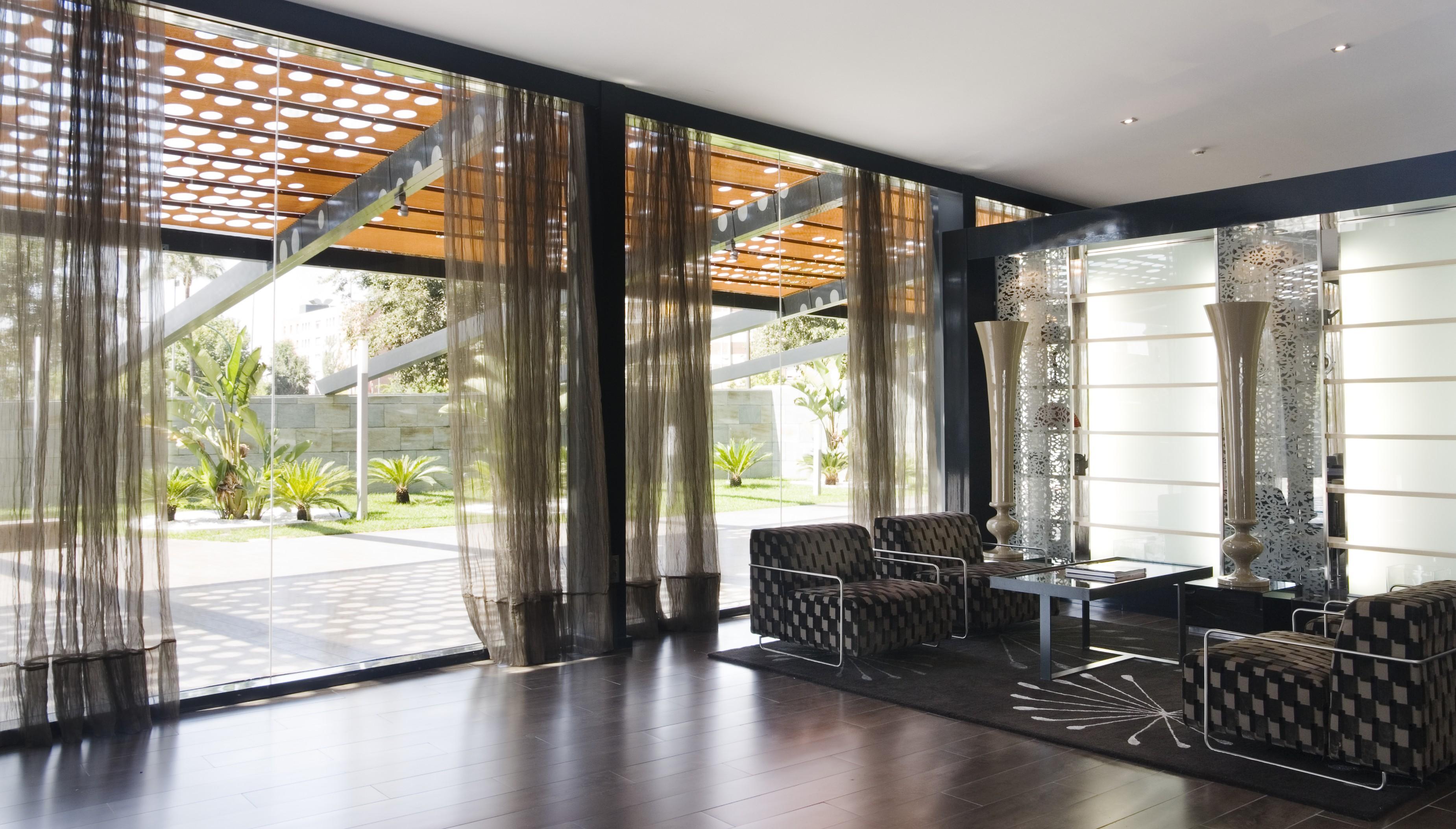 فندق يوروستارز بالاس قرطبة المظهر الخارجي الصورة The photo shows a modern interior space characterized by large windows that allow natural light to flood in. The floor is made of dark wood, which contrasts with the lighter tones of the furnishings. 

In the foreground, there are two stylish chairs 