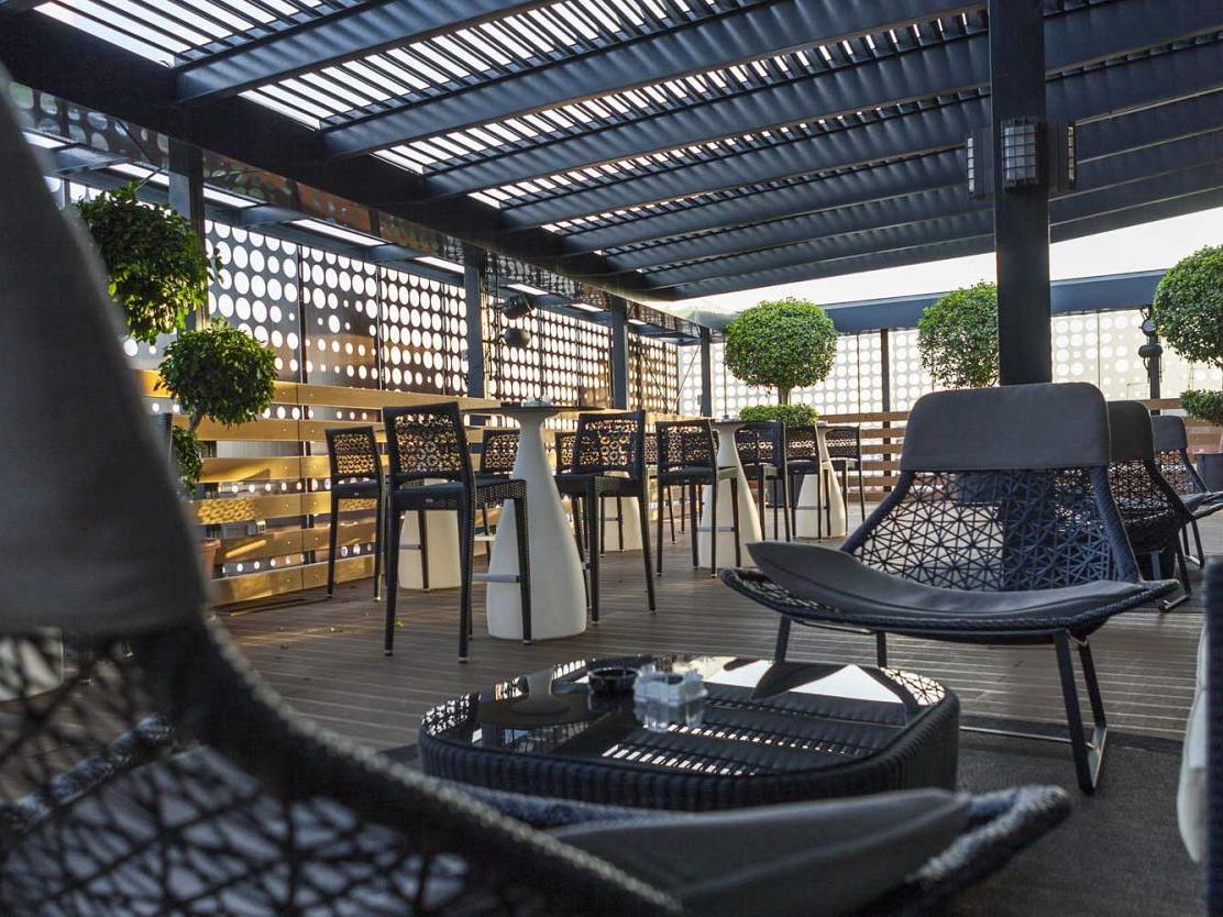 فندق يوروستارز بالاس قرطبة المظهر الخارجي الصورة The photo shows a modern outdoor seating area, likely on a rooftop or terrace. It features stylish black wicker chairs and tables arranged for comfort. The area is partially shaded by a striped overhead structure, creating a relaxing atmosphere. Pott