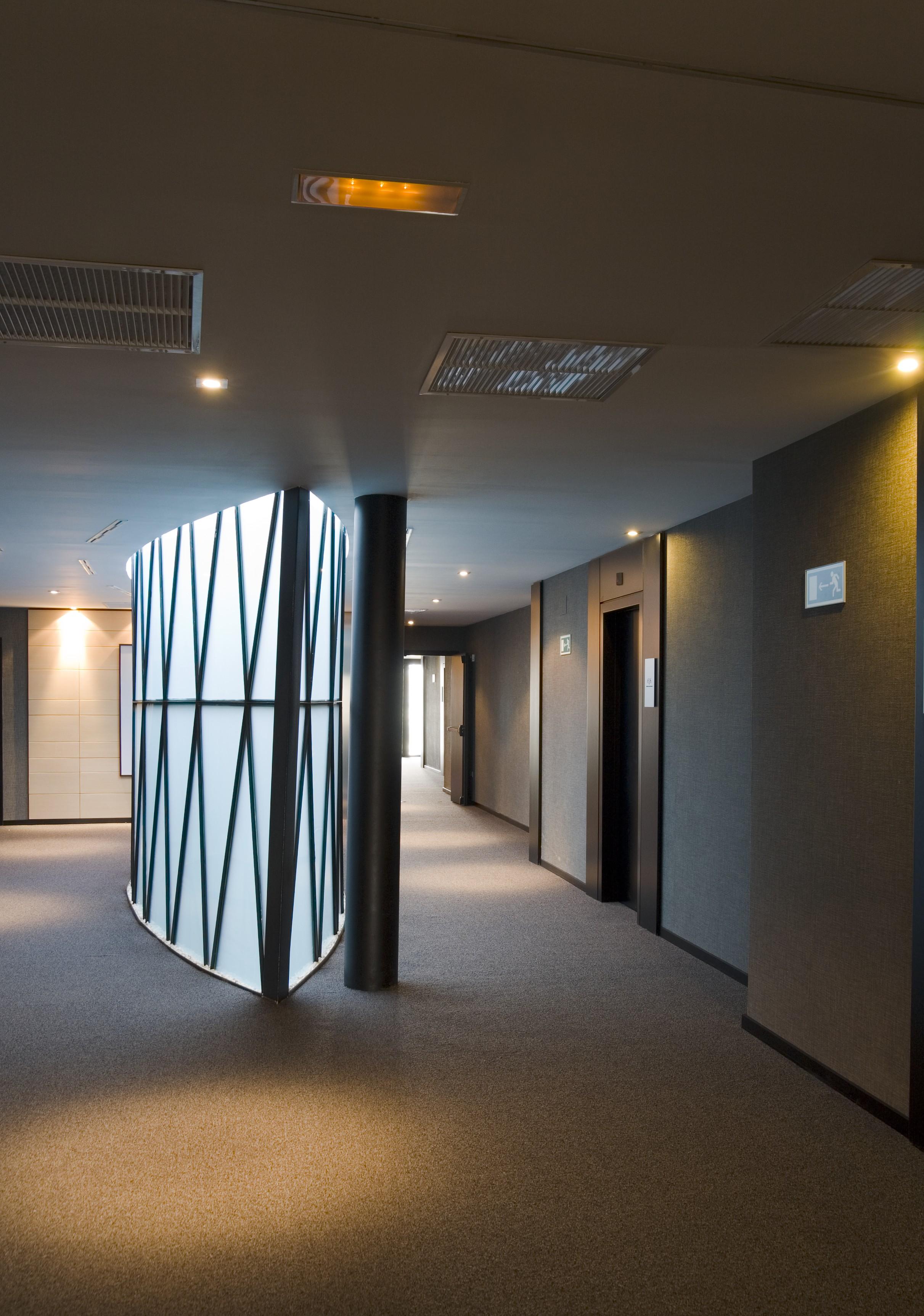 فندق يوروستارز بالاس قرطبة المظهر الخارجي الصورة The photo shows a modern indoor corridor featuring a smooth, curved wall with a geometric pattern. The corridor is well-lit with recessed ceiling lights, and the floor is carpeted. There are doors leading to elevators on the right side, and the walls