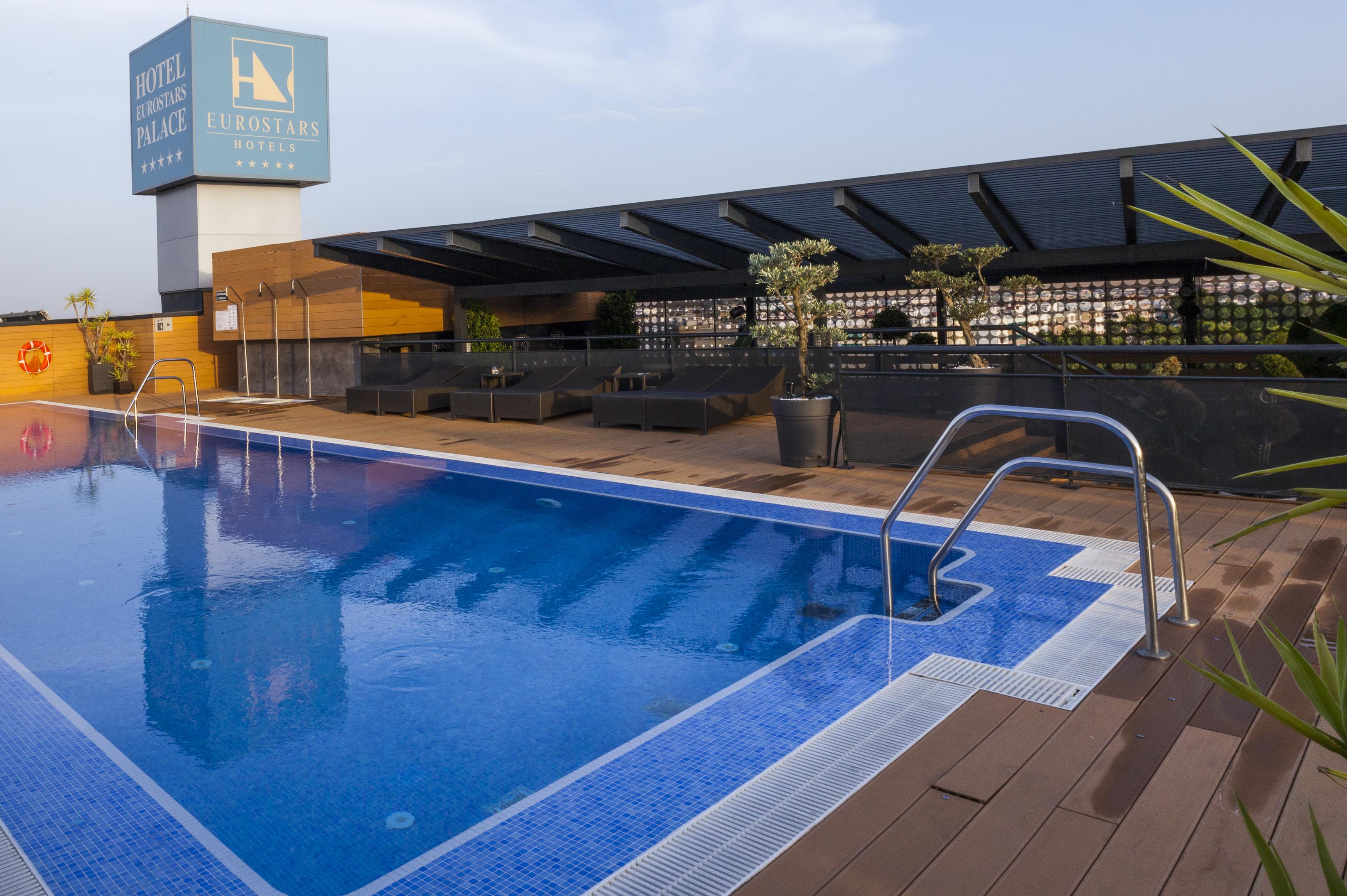 فندق يوروستارز بالاس قرطبة المظهر الخارجي الصورة The photo shows a rooftop swimming pool with a clear blue water surface. There is a section of the pool with a ladder for entry, and the surrounding area includes wooden decking. In the background, there is a sign for a hotel, which appears to be nam