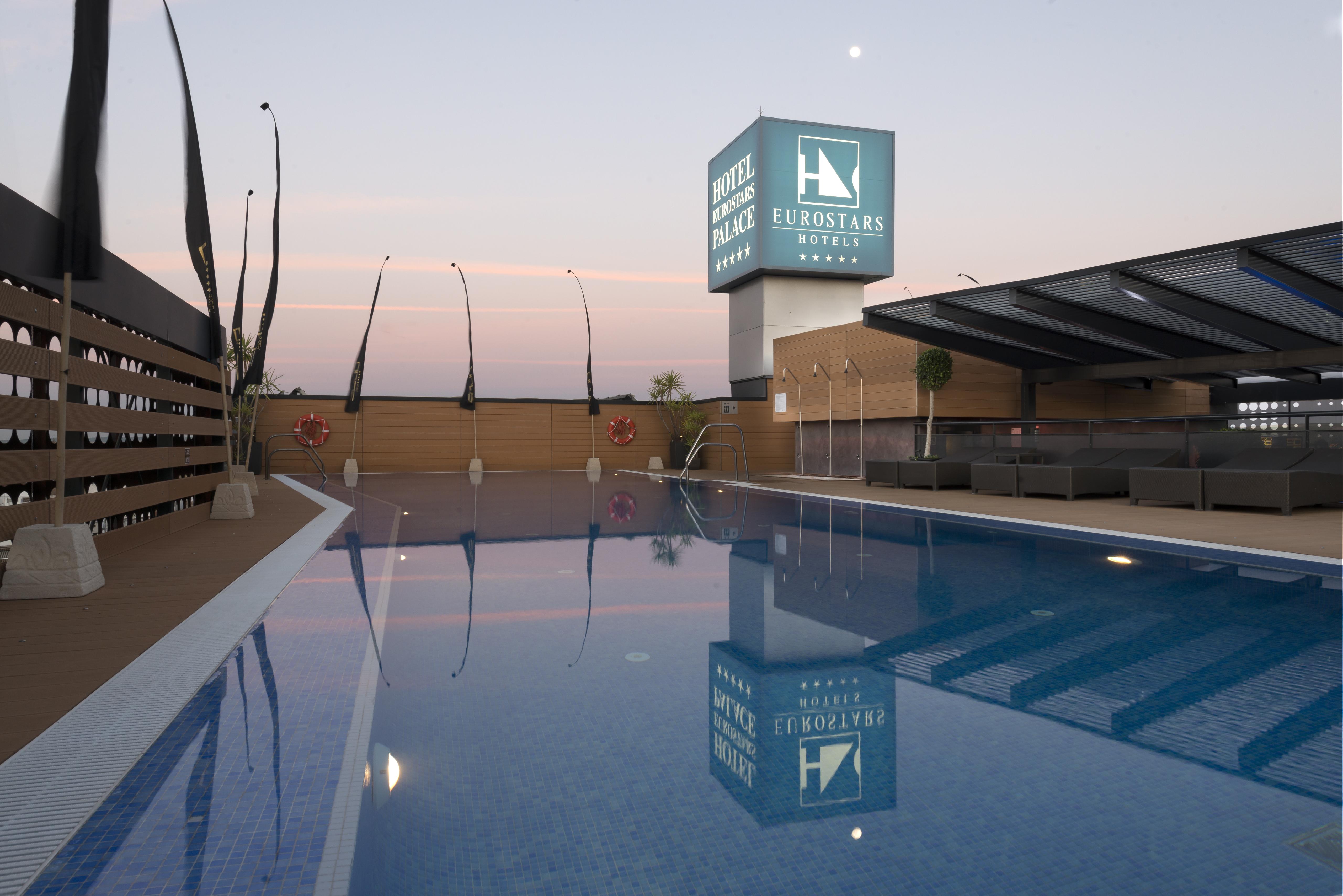 فندق يوروستارز بالاس قرطبة المظهر الخارجي الصورة The photo shows a rooftop space featuring a swimming pool. The pool has a clear blue water, and the area around it is designed with modern aesthetics, including a wooden deck and comfortable seating. In the background, there is a prominent sign for "