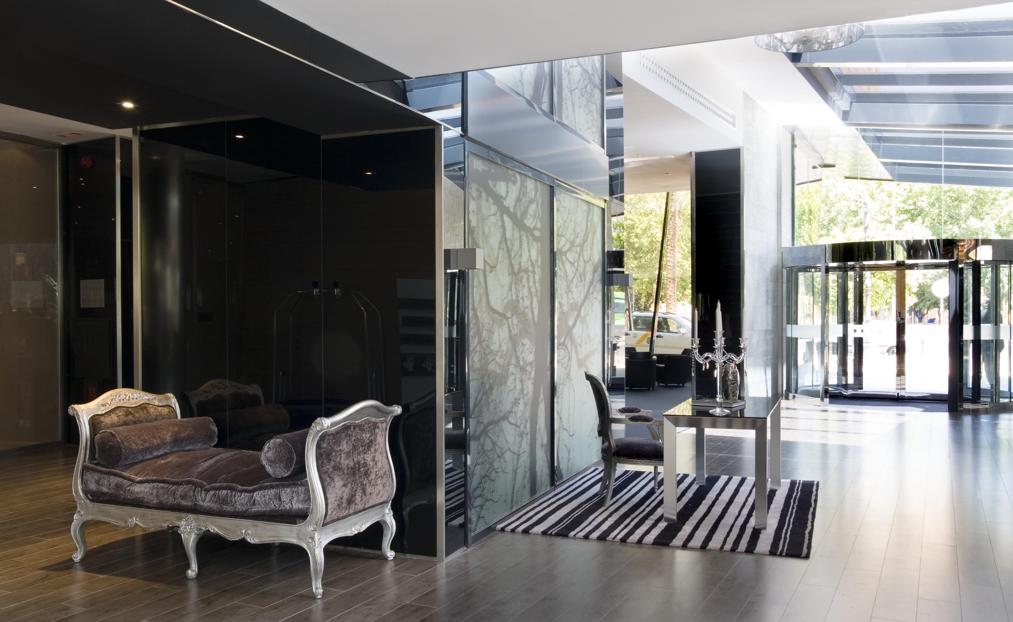 فندق يوروستارز بالاس قرطبة المظهر الخارجي الصورة The photo features a modern and stylish interior space, likely a lobby or reception area. On the left, there is an elegant couch with ornate detailing, set against dark, reflective walls. The floor is wooden and has a sleek design. To the right, ther