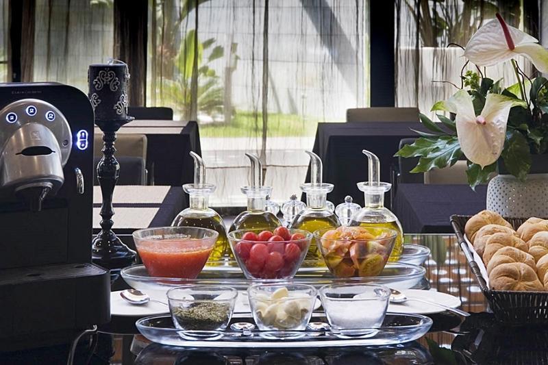فندق يوروستارز بالاس قرطبة المظهر الخارجي الصورة The photo displays a stylish breakfast or brunch spread on a table. In the foreground, several small glass containers hold various ingredients: there are glasses filled with different types of oil, a bowl of fresh red tomatoes, a bowl of mixed fruit,