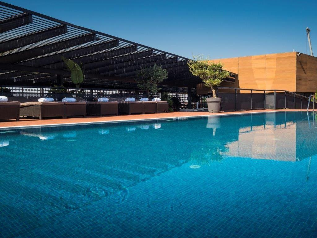 فندق يوروستارز بالاس قرطبة المظهر الخارجي الصورة The photo shows a rooftop swimming pool with a clear, vibrant blue surface reflecting the sky. Surrounding the pool are comfortable lounge chairs, some shaded by a modern overhead structure. The area is accented with potted plants, adding greenery to