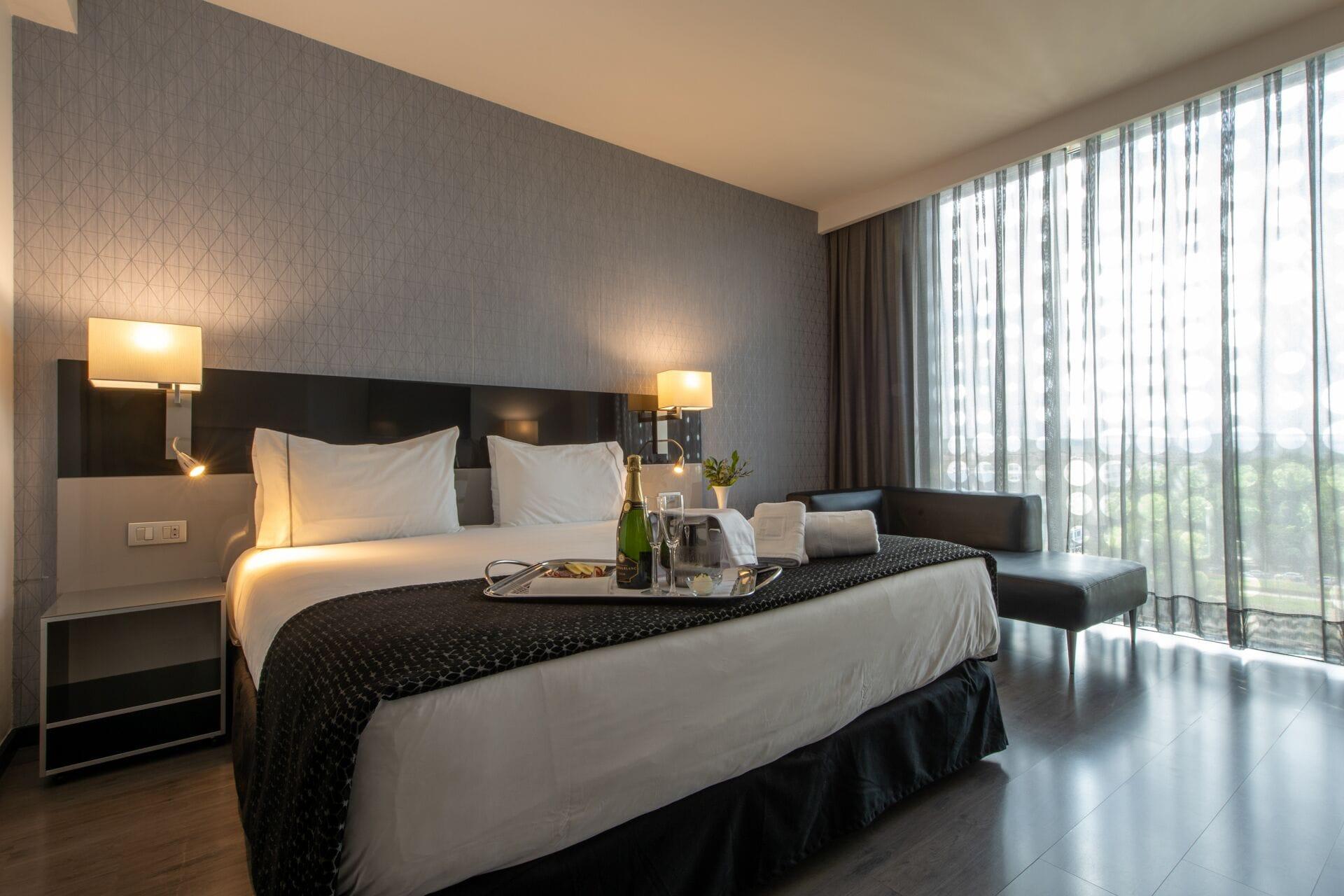 فندق يوروستارز بالاس قرطبة المظهر الخارجي الصورة The photo shows a modern hotel room featuring a large bed with crisp white linens and dark throw blankets. On either side of the bed, there are bedside lamps providing soft lighting. The room has a sleek design with a neutral color palette, including