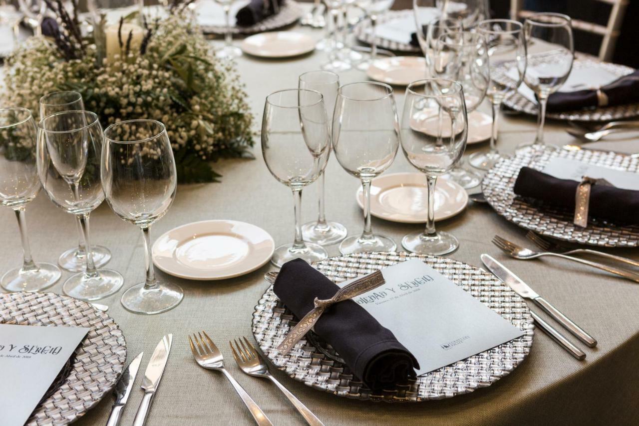 فندق يوروستارز بالاس قرطبة المظهر الخارجي الصورة The photo shows a beautifully arranged dining table set for an event. The table has a neutral-colored tablecloth and is adorned with elegant place settings. Each setting features a decorative plate with a textured silver charger underneath, and a fol